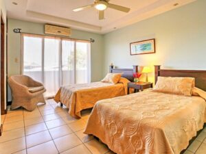 Bright guest bedroom with two twin beds, air conditioning, built-in closets, large window with greenery view, and en-suite bathroom.